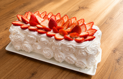 Imagem mostra uma fatia de bolo de Ninho com morango, massa branca, creme claro e pedaços de morango fresco no recheio.
