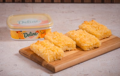 Pedaços de bolo de macaxeira com coco ralado e margarina Deline em tábua de madeira