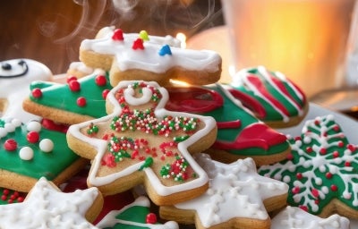 Em cima de uma mesa, prato redondo com biscoitos em formato de estrelas e árvore de Natal, decorados com glacê colorido e confeitos coloridos na cores vermelho, verde e branco. Em cima de uma mesa, prato redondo com biscoitos em formato de estrelas e árvore de Natal, decorados com glacê colorido e confeitos coloridos na cores vermelho, verde e branco.