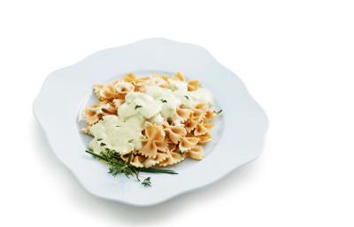 Fotografia em tons de amarelo em um fundo branco com um prato raso branco ao centro e o macarrão ao creme de ricota e ervas dentro.