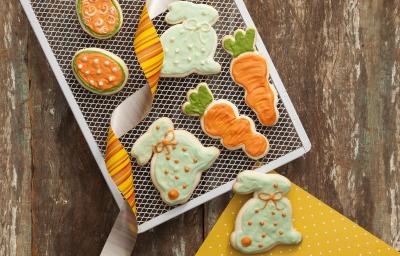 fotografia em tons de marrom, laranja e branco de uma bancada marrom vista de cima, contém uma grade branca com biscoitinhos nas cores laranja e branco no formato de cenoura e coelhos fotografia em tons de marrom, laranja e branco de uma bancada marrom vista de cima, contém uma grade branca com biscoitinhos nas cores laranja e branco no formato de cenoura e coelhos
