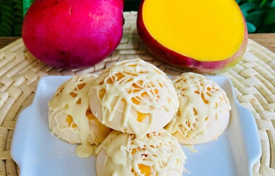 Fotografia mostra bombons de manga cobertas de chocolate branco. No mesmo cenário há duas mangas, sendo uma metade aberta.