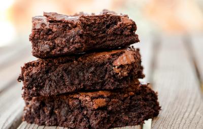 Fotografia de três pedaços de brownie sobrepostos sobre uma mesa de madeira clara. Fotografia de três pedaços de brownie sobrepostos sobre uma mesa de madeira clara.