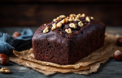 Bolo de chocolate recém-assado, com uma cor rica e escura, coberto com nozes. Ele está sobre papel em uma superfície de madeira rústica.
