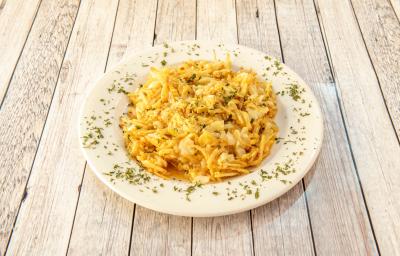 Fotografia de um bacalhau desfiado gratinado com batata palha, ovos batidos e requeijão. O bacalhau está em um prato branco fundo com salsinha picada e salpicada.