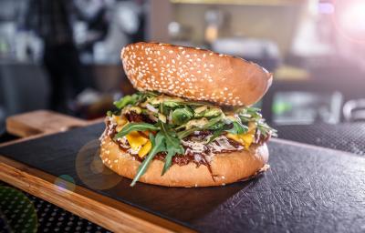Fotografia de um hamburguer de carne e champignon temperado e servido com rúcula. A fatia do pão na parte de cima, está ao contrário, e o lanhe está sobre uma tábua de madeira com fundo preto. Fotografia de um hamburguer de carne e champignon temperado e servido com rúcula. A fatia do pão na parte de cima, está ao contrário, e o lanhe está sobre uma tábua de madeira com fundo preto.