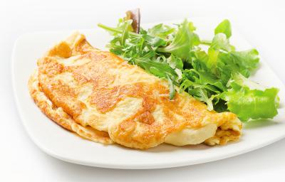 Fotografia de um omelete com crosta de queijo crocante dobrado ao meio, ao lado de uma salada de folhas, sobre um prato de vidro branco. O prato está sobre uma mesa branca. Fotografia de um omelete com crosta de queijo crocante dobrado ao meio, ao lado de uma salada de folhas, sobre um prato de vidro branco. O prato está sobre uma mesa branca.