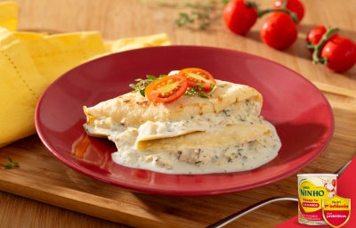 Crepe com recheio cremoso de palmito coberto com molho claro e decorado com tomate cereja, em mesa de madeira