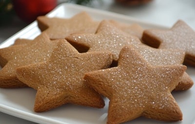 Em cima de uma mesa, prato redondo com biscoitos em formato de estrelas, decorados com açúcar cristal.