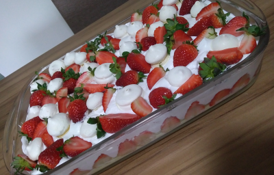 Foto em tons de vermelho da receita de merengue de morango com suspiros servida em uma travessa de vidro grande com morangos e suspiros por cima decorando. A receita está sobre uma mesa de madeira Foto em tons de vermelho da receita de merengue de morango com suspiros servida em uma travessa de vidro grande com morangos e suspiros por cima decorando. A receita está sobre uma mesa de madeira