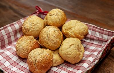 Fotografia de pãezinhos com massa de requeijão e queijo parmesão. Os pães estão dentro de uma cestinha quadrada com papel quadriculado vermelho e branco, que está sobre uma mesa de madeira.