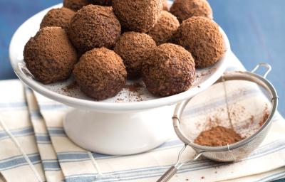 Fotografia em tons de azul em uma bancada de madeira azul clara, um pano branco listrado, um suporte branco com várias trufas de iogurte com chocolate. Fotografia em tons de azul em uma bancada de madeira azul clara, um pano branco listrado, um suporte branco com várias trufas de iogurte com chocolate.