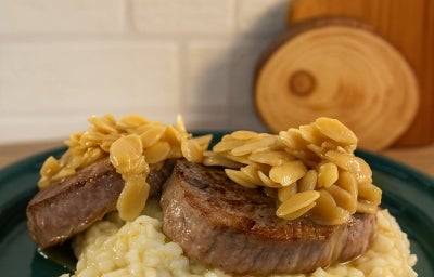 imagem mostra um prato de risoto cremoso em tons beges e por cima 2 medalhões de filé mignon com amendoas laminadas e um molho amanteigado por cima. imagem mostra um prato de risoto cremoso em tons beges e por cima 2 medalhões de filé mignon com amendoas laminadas e um molho amanteigado por cima.