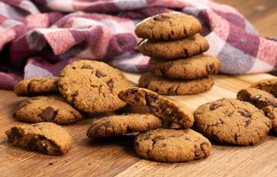 fotografia em tons de marrom, vinho e roxo de uma bancada marrom vista de frente, contém diversos biscoitos de chocolate espalhados pela mesa, e ao fundo um pano xadrez em tons de vinho e roxo. fotografia em tons de marrom, vinho e roxo de uma bancada marrom vista de frente, contém diversos biscoitos de chocolate espalhados pela mesa, e ao fundo um pano xadrez em tons de vinho e roxo.