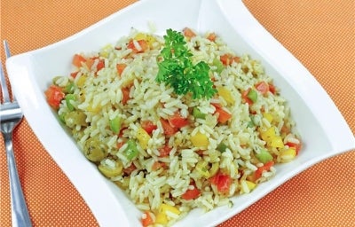 Em um prato branco, há arroz soltinho com uma mistura de legumes, como cenoura, ervilhas, milho, e pimentões, decorado com folhas de salsinha.