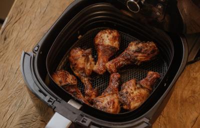 Fotografia em tons de marrom de uma bancada de madeira sobre ela o cesto da airfryer com 6 coxas de frango Fotografia em tons de marrom de uma bancada de madeira sobre ela o cesto da airfryer com 6 coxas de frango