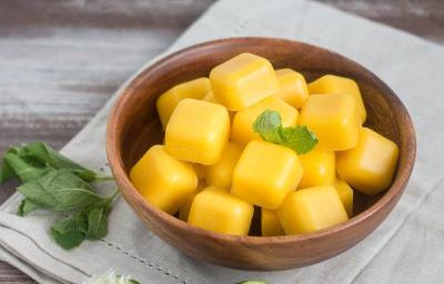 Fotografia em tons de amarelo em uma bancada de madeira, com um pano verde claro com um prato redondo de madeira com as balas cremosas de manga. Ao lado, limões espremidos e folhas de hortelã. Fotografia em tons de amarelo em uma bancada de madeira, com um pano verde claro com um prato redondo de madeira com as balas cremosas de manga. Ao lado, limões espremidos e folhas de hortelã.