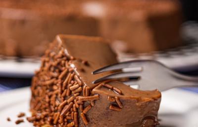 Foto da receita de Brigadeirão Sem Lactose. Observa-se uma fatia do Brigadeirão bem perto com chocolate granulado sendo cortada por um garfo. Foto da receita de Brigadeirão Sem Lactose. Observa-se uma fatia do Brigadeirão bem perto com chocolate granulado sendo cortada por um garfo.