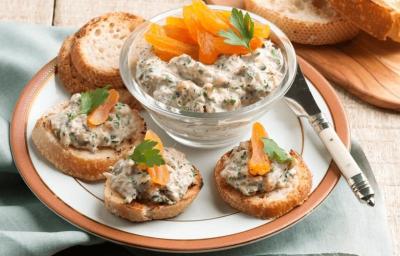 Fotografia em tons de laranja em uma bancada de madeira com um pano cinza, um prato branco com detalhes laranja vários canapés com patê de atum e damasco. Ao centro, um potinho de vidro com o patê de atum e damasco. Fotografia em tons de laranja em uma bancada de madeira com um pano cinza, um prato branco com detalhes laranja vários canapés com patê de atum e damasco. Ao centro, um potinho de vidro com o patê de atum e damasco.