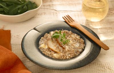 Foto da receita de risoto de pera com brie servida em um prato fundo azul com um garfo de madeira na borda e um copo de vidro com vinho branco ao fundo Foto da receita de risoto de pera com brie servida em um prato fundo azul com um garfo de madeira na borda e um copo de vidro com vinho branco ao fundo