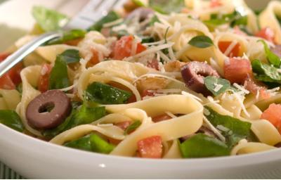 fotografia em tons de branco, verde e amarelo tirada de um recipiente redondo branco com macarrão, rúcula e pedaços de azeitona fotografia em tons de branco, verde e amarelo tirada de um recipiente redondo branco com macarrão, rúcula e pedaços de azeitona