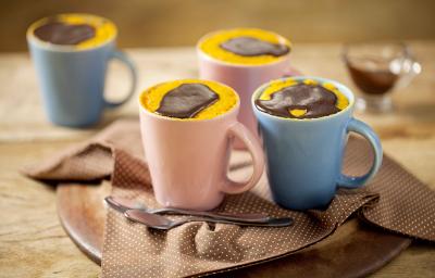 Canecas nas cores azul e rosa comporta o bolo de cenoura. As canecas estão em cima de uma mesa de madeira e um pano marrom. Canecas nas cores azul e rosa comporta o bolo de cenoura. As canecas estão em cima de uma mesa de madeira e um pano marrom.