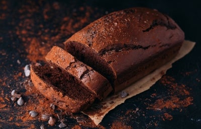 Em cima de uma mesa, bolo de chocolate cortado em duas fatias, polvilhado com cacau em pó.