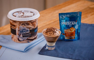Taça com sorvete de chocolate ao lado de um pote de sorvete e de um sachê de NESCAFÉ® Ice.
