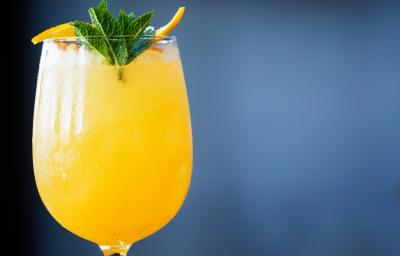 Foto da receita de G&T Wild, na cor em tom amarelada, servida numa taça de vidro e decorada com hortelã.