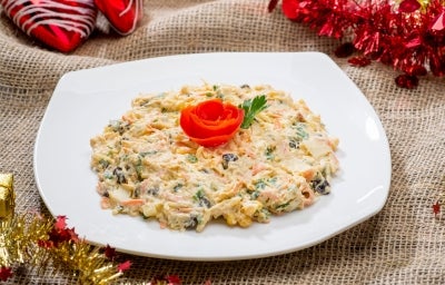 Em cima de uma mesa, prato com frango desfiado, cenouras raladas, milho e uvas-passas, decoradas com folhas de cheiro-verde e folho feita com cenoura. Em cima de uma mesa, prato com frango desfiado, cenouras raladas, milho e uvas-passas, decoradas com folhas de cheiro-verde e folho feita com cenoura.