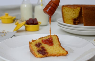 Prato branco com uma fatia de bolo de fubá com goiabada com uma colher derramando calda de goiabada.