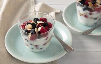 Foto em tons de azul claro da receita de parfait de iogurte com frutas vermelhas servida em dois copos altos sobre pratos pequenos azuis