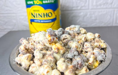 Fotografia em tons claros com um prato de pipoca doce ao centro. As pipocas são cobertas por leite NINHO em pó