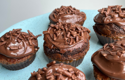 Fotografia mostra seis bolinhos de chocolate coberto por cobertura de chocolate granualdo dispostos em prato azul.