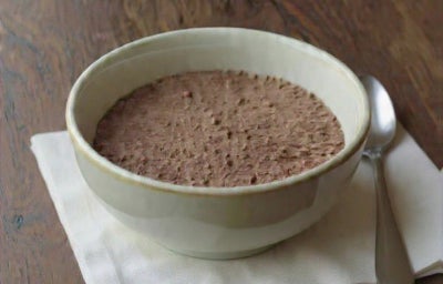 Fotografia em tons de marrom em uma bancada de madeira com um bowl ao centro e mousse de chocolate dentro.