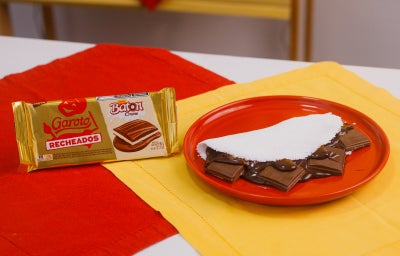 Tapioca recheada com creme de chocolate e Baton em prato vermelho, ao lado da embalagem do produto.