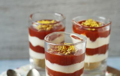 3 copinhos transparentes com Cheesecake de Limão Siciliano e Goiabada. Abaixo uma tábua de madeira redondo com um pano branco florido e 3 colheres para servir. 3 copinhos transparentes com Cheesecake de Limão Siciliano e Goiabada. Abaixo uma tábua de madeira redondo com um pano branco florido e 3 colheres para servir.