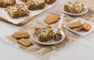 Foto da receita de Blondie de Tostines. Observa-se um prato de sobremesa com uma fatia de blondie com uma colher retirando uma fatia. Biscoitos TOSTINES decoram a foto. Foto da receita de Blondie de Tostines. Observa-se um prato de sobremesa com uma fatia de blondie com uma colher retirando uma fatia. Biscoitos TOSTINES decoram a foto.