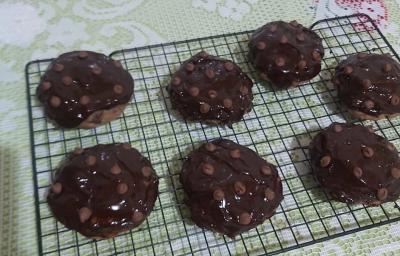 Foto da receita de Cookies low carb de chocolate. Observa-se uma grade preta com 7 cookies dispostos em cima, com calda de chocolate e chocolate em gotas na cobertura. Foto da receita de Cookies low carb de chocolate. Observa-se uma grade preta com 7 cookies dispostos em cima, com calda de chocolate e chocolate em gotas na cobertura.