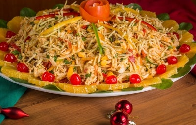 Em cima de uma mesa, prato de salpição colorido com frango desfiado, pimentões em tiras, milho-verde e batata-palha, decorado com laranja em rodelas, tomates e no topo do prato fio de cenoura em forma de flor. Em cima de uma mesa, prato de salpição colorido com frango desfiado, pimentões em tiras, milho-verde e batata-palha, decorado com laranja em rodelas, tomates e no topo do prato fio de cenoura em forma de flor.