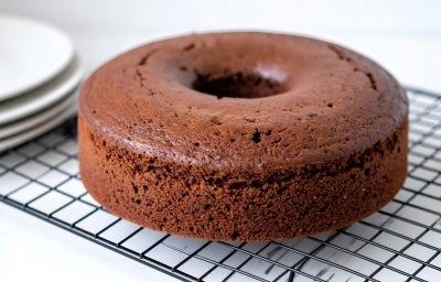 Em cima de uma mesa,  grade com bolo com furo no meio de chocolate fofinho.