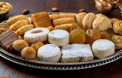 sobre uma mesa de madeira, uma bandeja de prata repleta de doces amanteigados e petit fours em diferentes formatos. Eles são pequenos, dourados, alguns com açúcar, outros com chocolate.