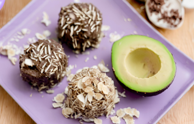 Fotografia em tons de roxo com um prato retangular roxo ao centro. Em cima do prato existe 3 brigadeiros de cor marrom e ao lado existe metade de um abacate. Todos os brigadeiros estão polvilhados com coco ralado Fotografia em tons de roxo com um prato retangular roxo ao centro. Em cima do prato existe 3 brigadeiros de cor marrom e ao lado existe metade de um abacate. Todos os brigadeiros estão polvilhados com coco ralado