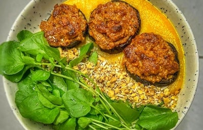 Fotografia vista de cima em tons claros de um prato claro de vidro com berinjela, queijo, molho de tomate, agrião e farofa. Fotografia vista de cima em tons claros de um prato claro de vidro com berinjela, queijo, molho de tomate, agrião e farofa.