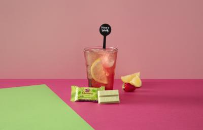 Foto da receita de Soda Italiana Pink Lemonade. Observa-se um fundo rosa e verde com um copo alto ao centro, servido cheio de gelo com uma rodela de limão siciliano dentro. À frente, um KIT KAT Limão.