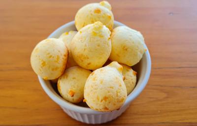Fotografia de um ramekin branco com vários pães de queijo. O recipiente está sobre uma mesa de madeira. Fotografia de um ramekin branco com vários pães de queijo. O recipiente está sobre uma mesa de madeira.