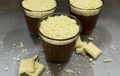 Foto da receita de trufa cremosa servida em três porções em copos de vidro baixos sobre uma mesa acinzentada com pedaços e raspas de chocolate branco rodeando os copos como decoração Foto da receita de trufa cremosa servida em três porções em copos de vidro baixos sobre uma mesa acinzentada com pedaços e raspas de chocolate branco rodeando os copos como decoração