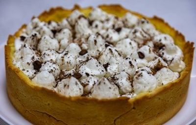 Em cima de uma mesa, banoffee com massa de biscoitos crocante, decorado com chantilly e canela em pó.