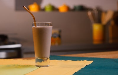 imagem mostra um copo de refresco roxo cremoso preparado com açaí e banana