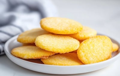 Em cima de uma mesa, prato redondo com biscoitos dourados, polvilhado com açúcar cristal. Em cima de uma mesa, prato redondo com biscoitos dourados, polvilhado com açúcar cristal.